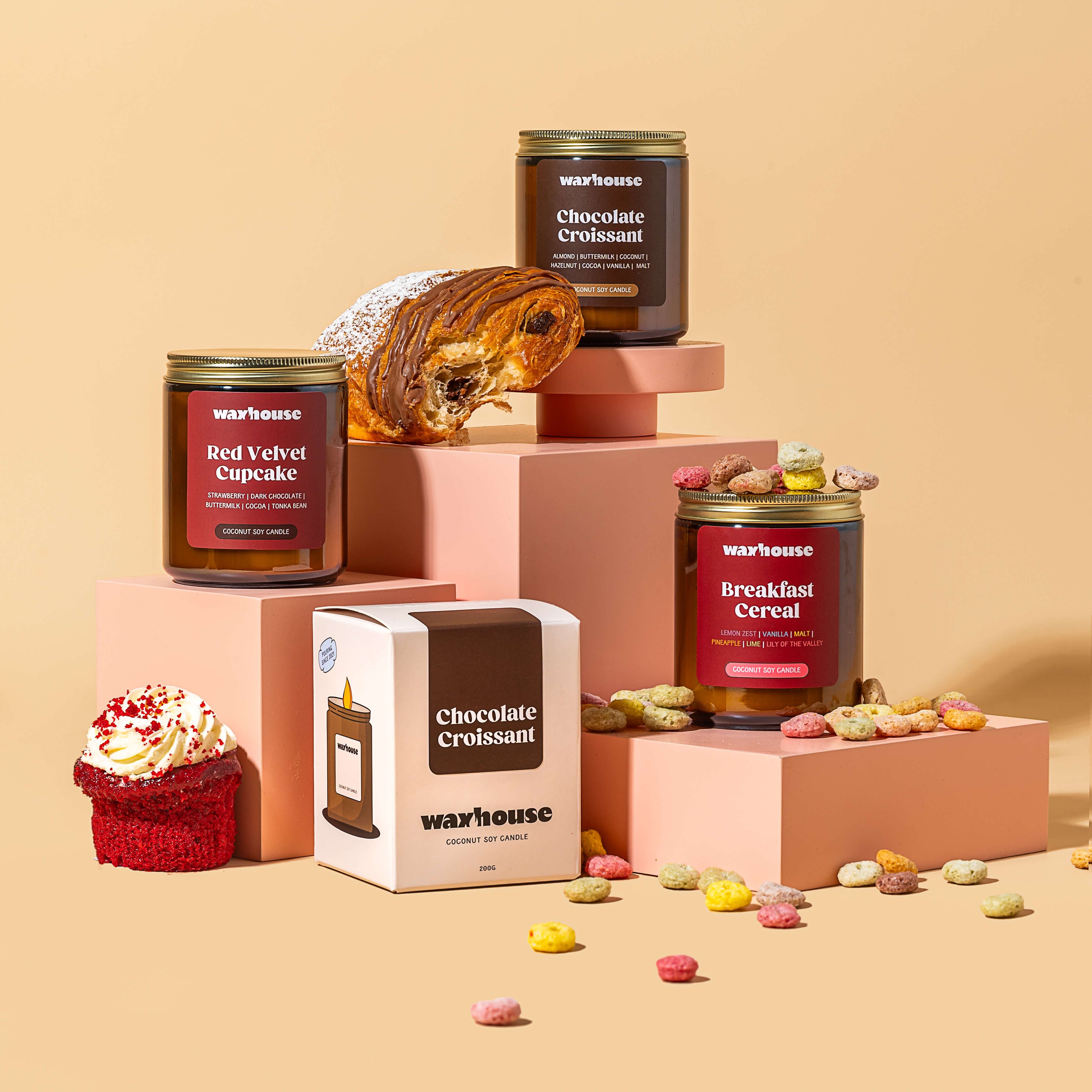 Assorted waxhouse candles including cakes, pastries, and cereal on a beige background